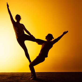 The two silhouettes of people practicing yoga in the sunset light