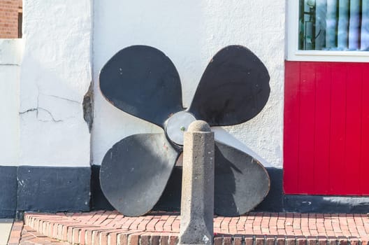 Large old ship screw stands in front of a house wall.