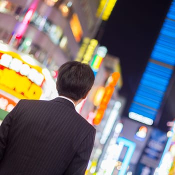 Solitary japanese corporative businessman in suit, after work, waiting on crossroad in Kabukicho, entertainment and red-light district in Shinjuku, Tokyo, Japan.