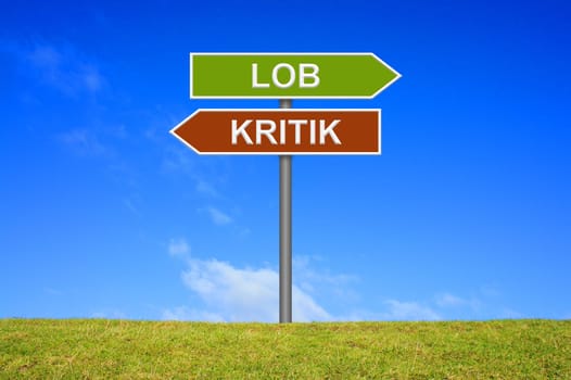 Signpost on a meadow in front of blue sky shows praise or criticism