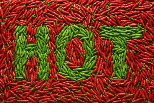 Word HOT written with green peppers, amid red peppers.
