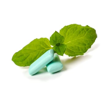 Two chewing gum with a leaf of mint on a white background