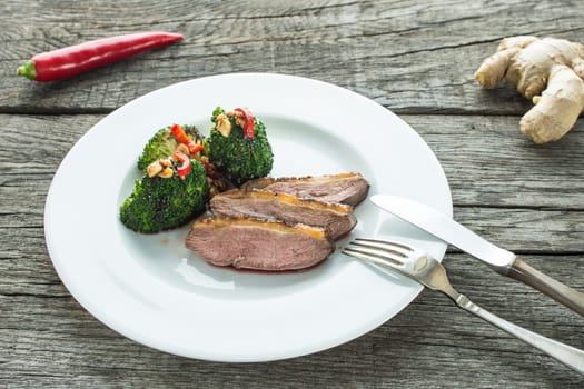 Plate of roasted duck breast and broccoli and chili