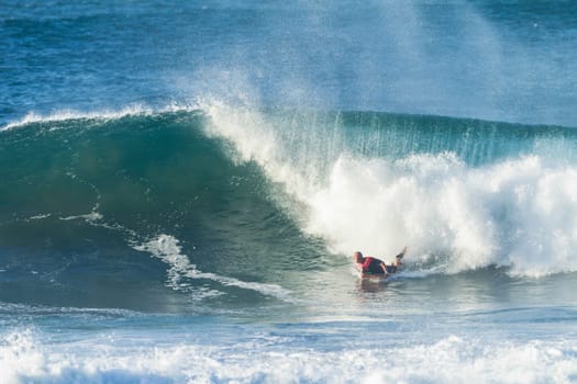 Surfing body-boarder rides large ocean wave
