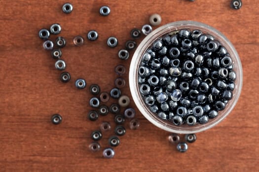 Shiny grey seed beads in a small container and on table, as seen from above.