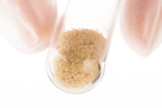 Brown crystals in test tube held by fingers on white background.