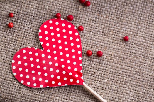 Paper heart decoration with white polka dots and red candy decorations on burlap.