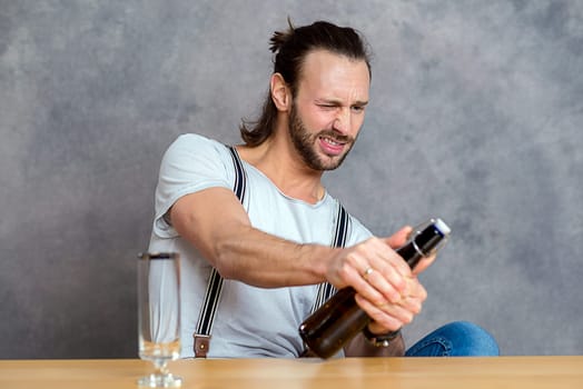 young man in front of gray background opening a beer bottle