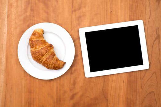 delicious croissant with tablet PC on wooden table from above