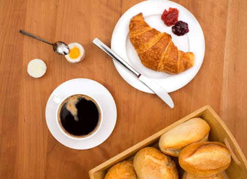 breakfast with croissant, bun, coffee and egg on wooden table