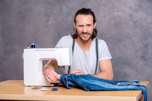 young tailor with sewing machine in front of gray background