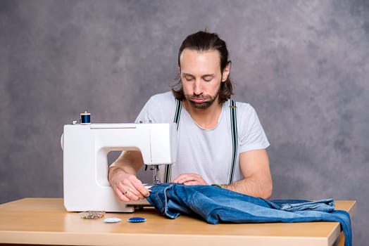 young tailor with sewing machine in front of gray background