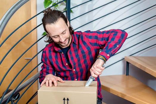 young man sitting in corridor and opening a package