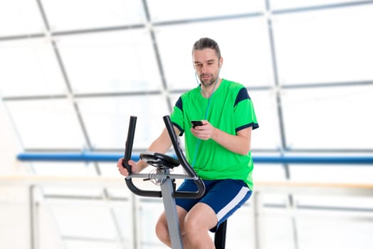 young man in green shirt train with fitness machine and listening music