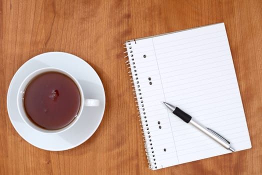 notepad with pen and a cup of tea on wooden table from above