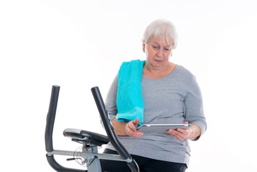 gray-haired female senior train with fitness machine and using tablet PC