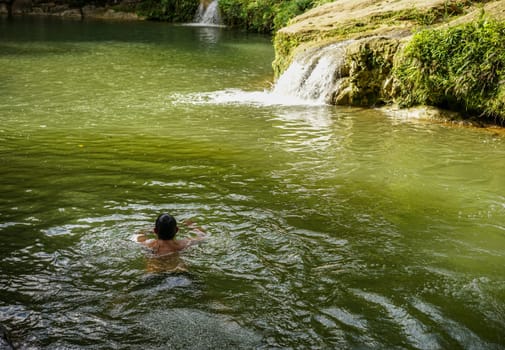 landscape with small waterfall by the lake and a swimming person on a summer day