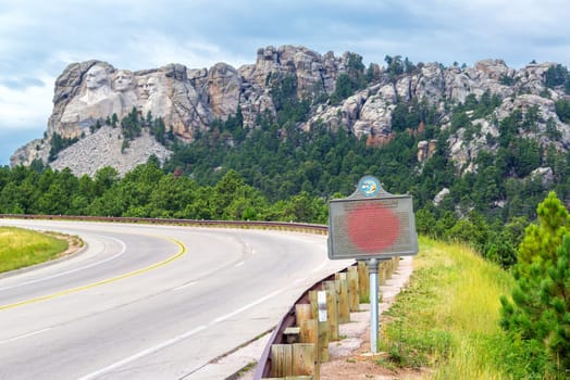 Highway leading to Mount Rushmore with a sign dedicated to Gutzon Borglum in the foreground