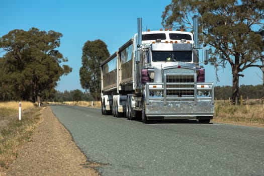 A large B-Double Semi Trailer driving down a deserted rural road.`