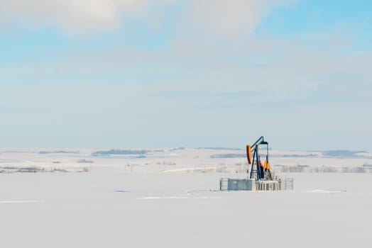 Landscape of a lone orange pumpjack in a snow covered field.