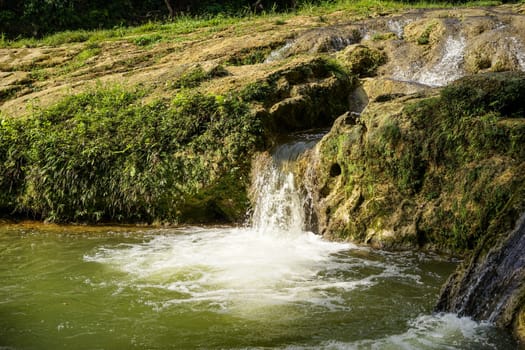 landscape with small waterfall by the lake on a summer day and green moss on the stones