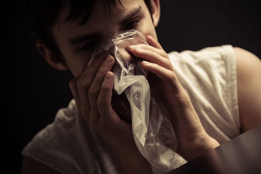 Close up of single male teenager inhaling narcotics from plastic re-sealable bag on his mouth