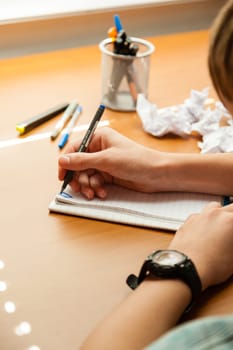 Over the shoulder view of unidentifiable young person wearing watch and writing on note pad next to crumpled up pieces of paper