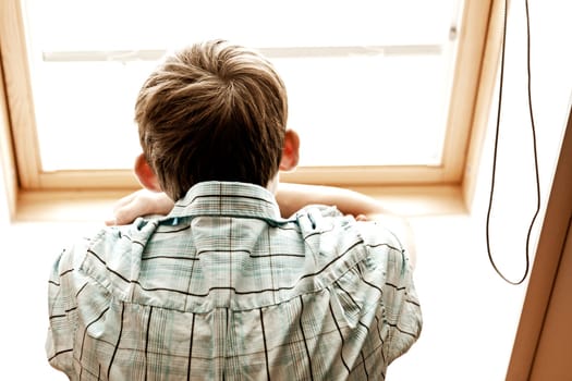 Rear view perspective of unidentifiable teenage male looking out into window from inside room