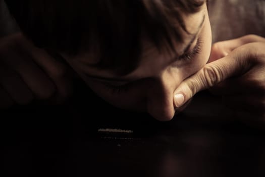 Close up of male teen putting finger on nostril as he snorts cocaine lines on table
