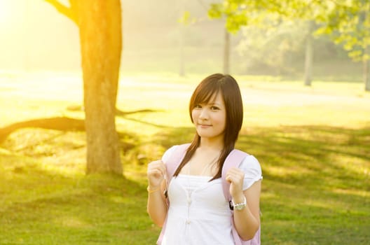 Young Asian college student standing on campus lawn, with backpack and smiling.