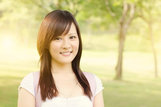 Young female Asian university student standing on campus lawn, with backpack and smiling.