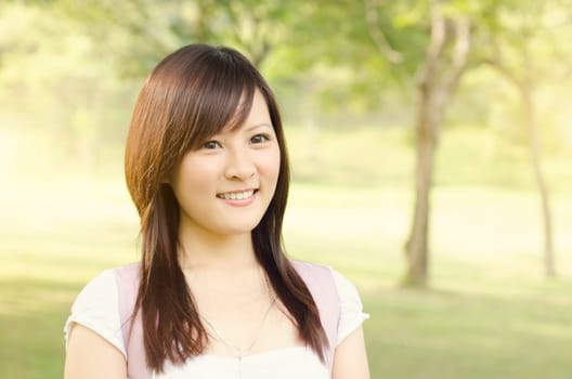 Young female Asian college student standing on campus lawn, with backpack and smiling.
