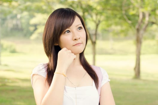 Young Asian college girl student standing on campus lawn, having a thought  and smiling.