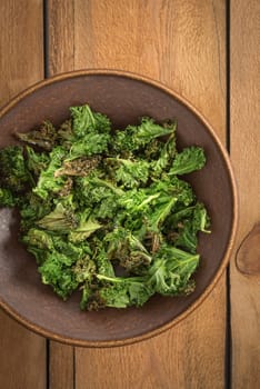 Kale chips with sea salt in a brown bowl on a wooden table