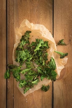 Kale chips with sea salt in parchment paper on wooden table