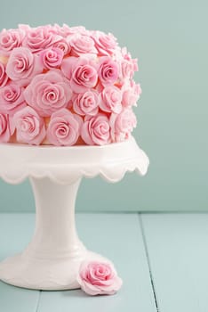 Ivory fondant covered cake with pink sugar roses on cake stand