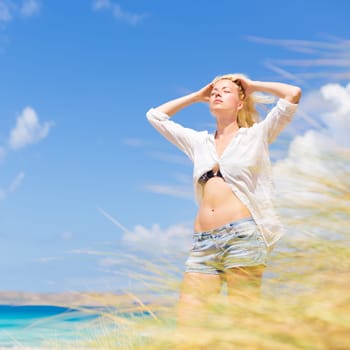 Relaxed woman enjoying freedom and life an a beautiful sandy beach.  Young lady feeling free, relaxed and happy. Concept of freedom, happiness, enjoyment and well being.  Enjoying Sun on Vacations.