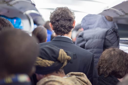 Interior of airplane with passengers queuing on the aisle, collecting their luggage to disembark plane.