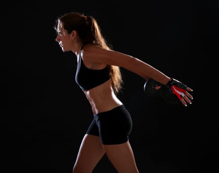 Young woman doing exercise with dumbbells, over black
