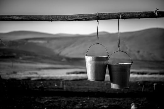 Pair of metal buckets hanigng from a rustic wooden beam