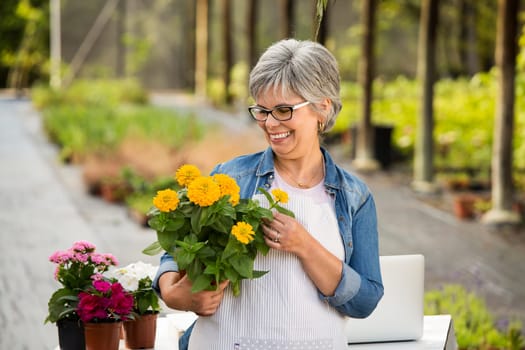 Beautiful mature woman working in a greenhouse holding flowers on her hands