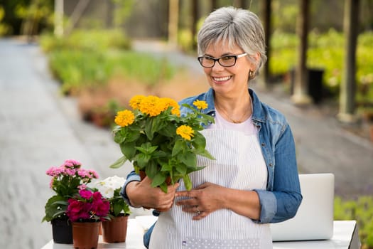 Beautiful mature woman working in a greenhouse holding flowers on her hands