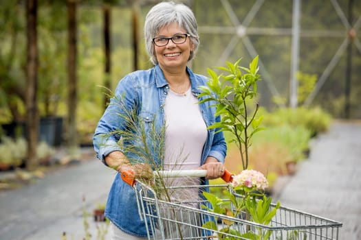 Beautiful mature woman working in a greenhouse holding flowers on her hands