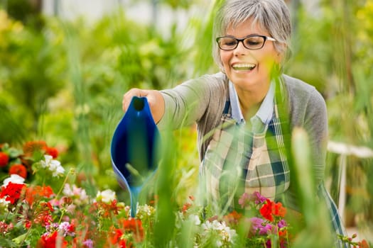 Beautiful mature woman working in a greenhouse holding flowers on her hands