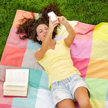 Smiling young woman lying on a blanket and making a selfie