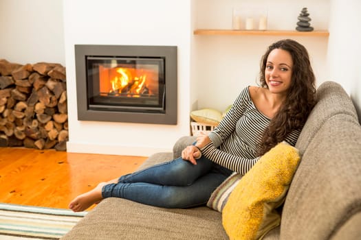 Beautiful woman drinking a hot tea at the warmth of the fireplace