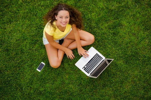 Beautiful young woman lying on the grass and working with a laptop
