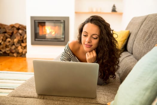 Beautiful woman working with a laptop at the warmth of the fireplace