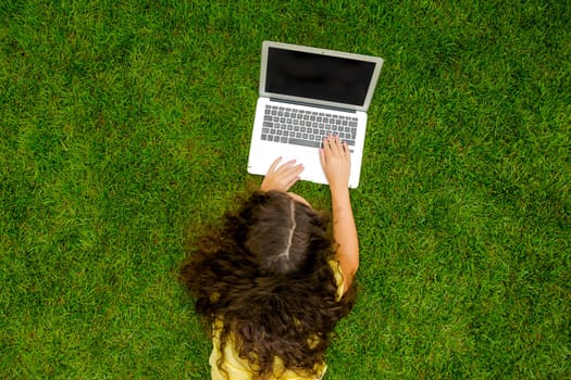 Beautiful young woman lying on the grass and working with a laptop
