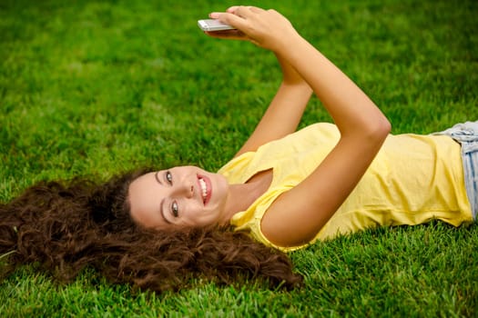 Smiling young woman lying on the grass and making a selfie